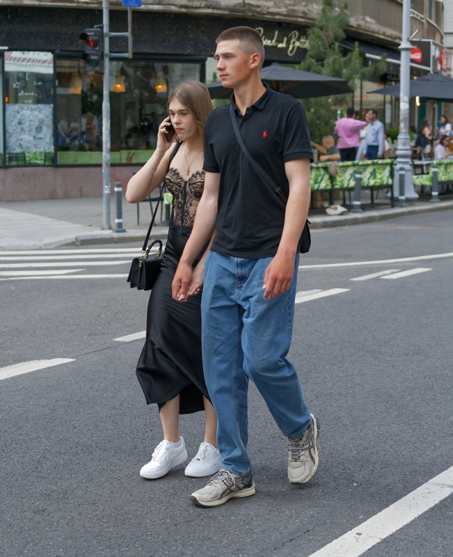 Woman dressed in a black lace corset top with a satin skirt walking with a man in blue jeans